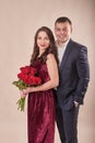 Valentine`s Day couple with roses on beige background. Portrait of happy young lovers with flowers. Picture showing man giving Royalty Free Stock Photo