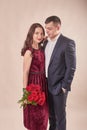 Valentine`s Day couple with roses on beige background. Portrait of happy young lovers with flowers. Picture showing man giving Royalty Free Stock Photo