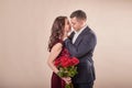 Valentine`s Day couple with roses on beige background. Portrait of happy young lovers with flowers. Picture showing man giving Royalty Free Stock Photo