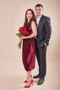 Valentine`s Day couple with roses on beige background. Portrait of happy young lovers with flowers. Picture showing man giving Royalty Free Stock Photo