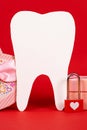 Valentine's Day in dentistry - a large white tooth, a heart and boxes of gifts on a red background, a place for text