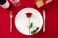 Valentine`s Day dining table with red rose flower on plate and cutlery on red background. Top view Royalty Free Stock Photo