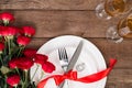 Valentine's Day dinner table setting with red ribbon, roses, knife and fork ring over oak background. Royalty Free Stock Photo