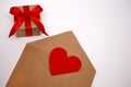 Valentine`s Day, February 14th red heart in an envelope on a white background, next to a gift in a package tied with a red ribbon Royalty Free Stock Photo