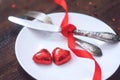 Valentine's Day Festive table setting, mockup with two red heart shape chocolate candies on white plate, fork, knife and red Royalty Free Stock Photo