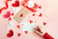 Valentines Day, a girl writes a love message on a pink background with paper hearts and a gift Royalty Free Stock Photo