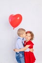 Valentine`s day kids. Boy kisses girl five years old holding red ball heart