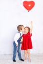 Valentine`s day kids. Boy kisses girl five years old holding red ball heart