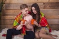 Valentine`s Day. Love story. Happy young couple, hugging each other, with hot mugs of tea under a plaid , against the background Royalty Free Stock Photo