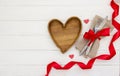 Valentine`s day place setting.Fork, knife and heart shape  wooden plate on a white wooden table.  Valentine`s Day or romantic Royalty Free Stock Photo