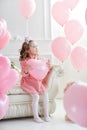 Beautiful preschool girl in a white studio with pink heart-shaped balloons