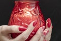 Valentine`s day, red candle in the hands. Red manicure. Black background. Candle fire in the dark