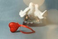 Valentine`s day, a red sparkling heart on the background of a statuette with kissing birds. With bokeh effect on a gray backgroun