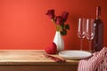 Valentine`s day romantic dinner concept. Wooden table with plate, wine bottle and rose flowers over red background Royalty Free Stock Photo