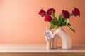 Valentine's day romantic still life with red rose bouquet in modern vase on wooden table over peach color background Royalty Free Stock Photo