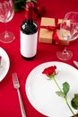 Valentine`s Day setting table. Cutlery, rose, gift box and wine bottle on red background Royalty Free Stock Photo