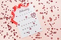 Valentine`s Day. Small red hearts highlight the date February 14 on a calendar sheet and a red ribbon on a pink heart-strewn Royalty Free Stock Photo