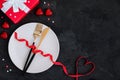 Valentine`s Day table setting with plate, gold knife, fork, red ribbon with heart and present box Royalty Free Stock Photo