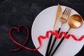 Valentine`s Day table setting with plate, gold knife, fork, spoon, red ribbon with heart Royalty Free Stock Photo