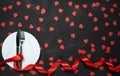 Valentine`s day table setting with plate, knife, fork, red ribbon and hearts on festive black background. a gift to your beloved Royalty Free Stock Photo