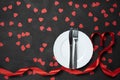 Valentine`s day table setting with plate, knife, fork, red ribbon and hearts on festive black background. a gift to your beloved Royalty Free Stock Photo