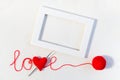 Valentine`s day or wedding backdrop. Red knitted volume heart in word love, ball of thread and white frame on knitted Royalty Free Stock Photo