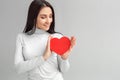 Valentine`s Day. Woman standing isolated on gray looking at heart card smiling pensive Royalty Free Stock Photo