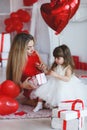 Valentine`s Day - young mother and little daughter in a room on the floor with gifts on a background of red heart-shaped balloons