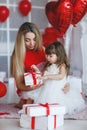 Valentine`s Day - young mother and little daughter in a room on the floor with gifts on a background of red heart-shaped balloons