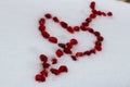 Valentine`s heart shape with arrow made by pomegranate seeds on white snow.