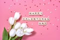 Valentine sign on wooden cubes and white tulip flower on pink background. Love and Valentine day concept. Royalty Free Stock Photo