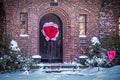 Valentine wreath of rustic arched wooden door set in brick arch in vine covered house on snowy winter day