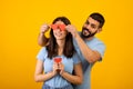 Valentine's holiday celebration. Loving arab husband covering wife's eyes with paper hearts, yellow background