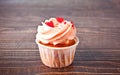 Valentines cupcake cream cheese frosting decorated with heart shaped candy on the wooden background.