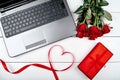 Valentines Day background with bouquet of red roses, ribbon shaped as heart, gift box and open laptop computer, copy space. Love Royalty Free Stock Photo