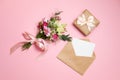 Valentines day composition: bouquet of flowers, gift box with ribbon bow, kraft envelope with greeting card lay at pink background