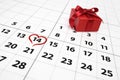 Valentines day concept - close up of calendar with red heart shaped marked 14th february dating and red gift box with shiny ribbon Royalty Free Stock Photo