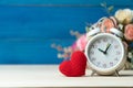 Valentines day concept. hand make yarn red heart beside white alarm clock in front of rose flower bouquet on wooden table and blue