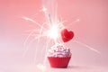 Valentines day cupcake. Cupcake with pink cream and sprinkled, with red heart and sparkler on a pink background. Concept postcard Royalty Free Stock Photo