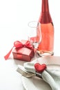 Valentines day dinner with table place setting with red gift, glass for champagne, a bottle of champagne, heart ornaments with sil Royalty Free Stock Photo