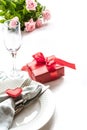 Valentines day dinner with table place setting with red gift, glass for champagne, heart ornaments with silverware on white. Close Royalty Free Stock Photo