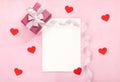 Valentines day greeting card with pink gift box, white bow, long curved ribbon and paper red hearts.
