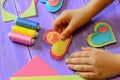 Kid holds a felt heart in his hand. Kid made a felt heart. Colorful felt hearts, scissors, thread on a wooden table Royalty Free Stock Photo