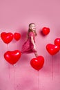 Valentines day. Little cute girl jumping with red heart balloons on pink background Royalty Free Stock Photo