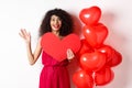 Valentines day and love concept. Cheerful young woman in elegant red dress, standing near romantic balloons and holding Royalty Free Stock Photo