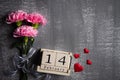 Valentines day and love concept. Pink carnation flower with February 14 text on wooden block calendar and red heart and on gray