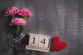 Valentines day and love concept. Pink carnation flower with February 14 text on wooden block calendar and red heart and on gray