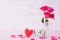 Valentines day and love concept. Pink roses in vase with February 14 text on wooden block calendar on white wooden background
