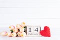 Valentines day and love concept. Pink tulips in vase with handmade red heart and February 14 text on wooden block on white wooden
