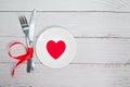 Valentines day meal background with red ribbon, hearts, fork, knife, white plate and napkin. Romantic holiday table Royalty Free Stock Photo